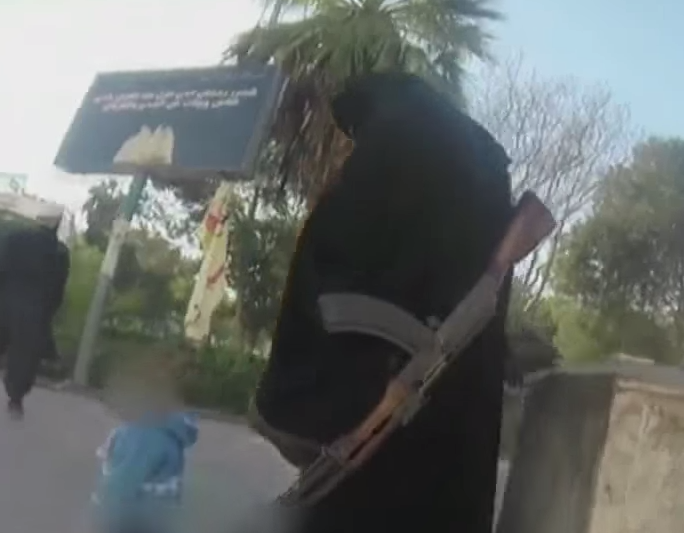 A Syrian woman with an AK-47 walks with her child 