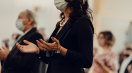 Woman in church wearing a face mask and praying with her hands outstretched