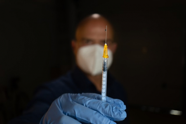 syringe held in hand by man wearing mask and gloves