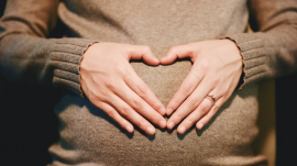 pregnant mom forming a heart shape with her hands above her womb where a baby is growing