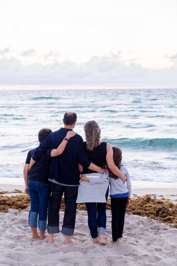 family of four standing on the beach facing the sea