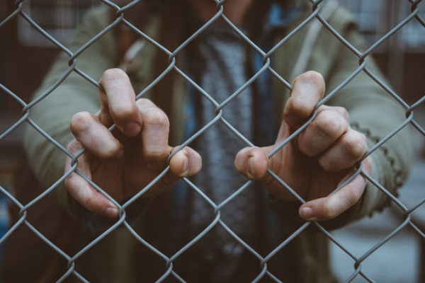 jailed man holding chain link fence with hands.