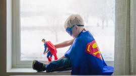 Young boy wearing Superman costume playing with Superman toy