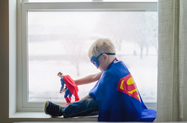 Young boy wearing Superman costume playing with Superman toy