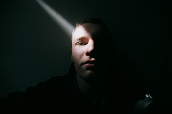 emotionless man sitting in the dark with a beam of light hitting his face
