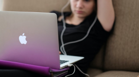 teen watching on a macbook beside her phone